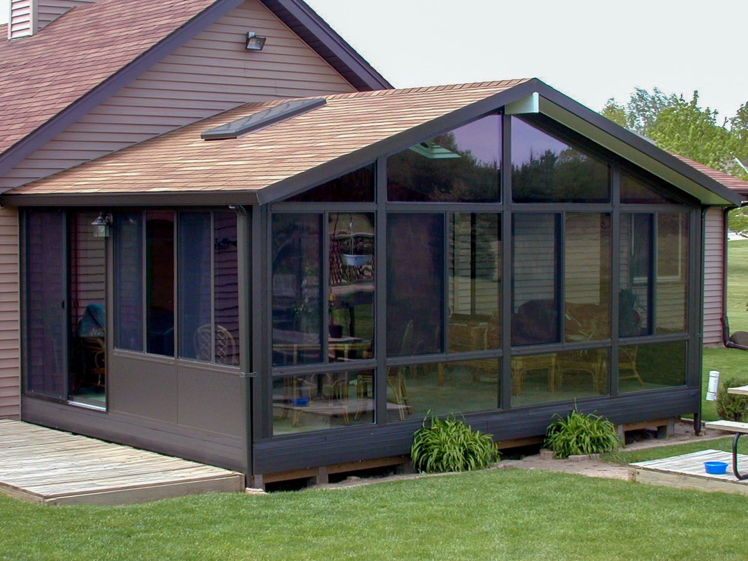 Custom dark-framed all-season room addition with insulated glass walls, skylight, and cathedral ceiling attached to a residential home.