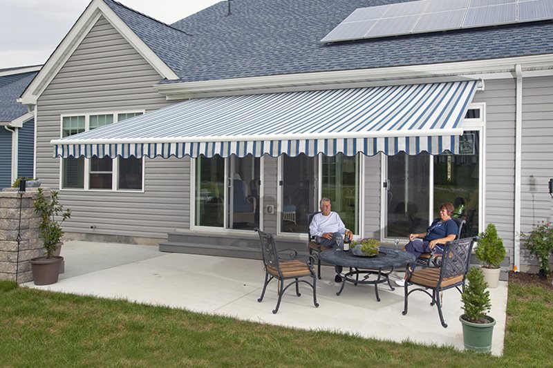 A home patio featuring a custom blue and white striped motorized retractable awning providing shade for two people sitting at a patio table.