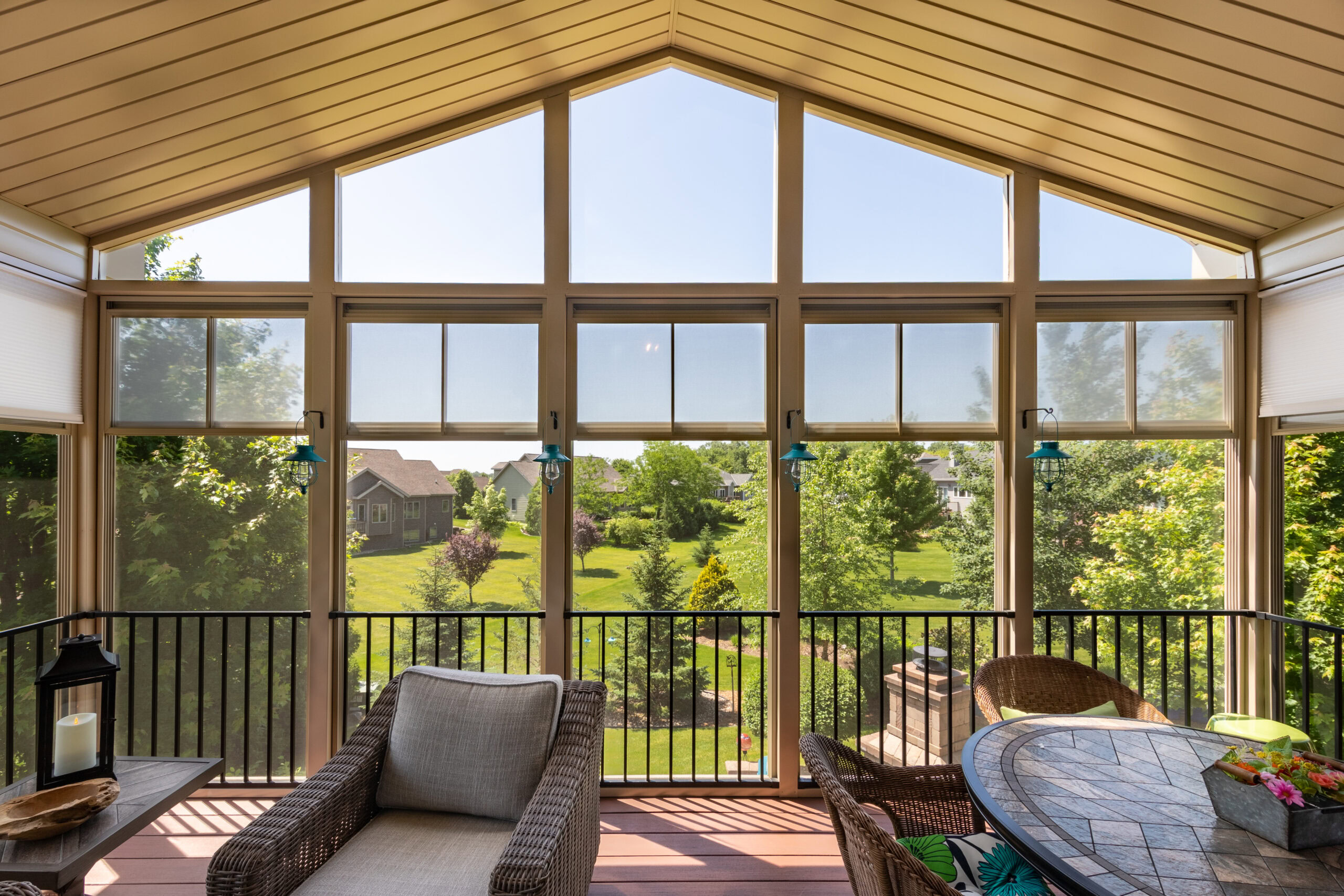 Interior view of a 3-season vinyl porch enclosure by Kool View featuring vaulted ceilings, wicker furniture, and large clear windows overlooking a green yard.